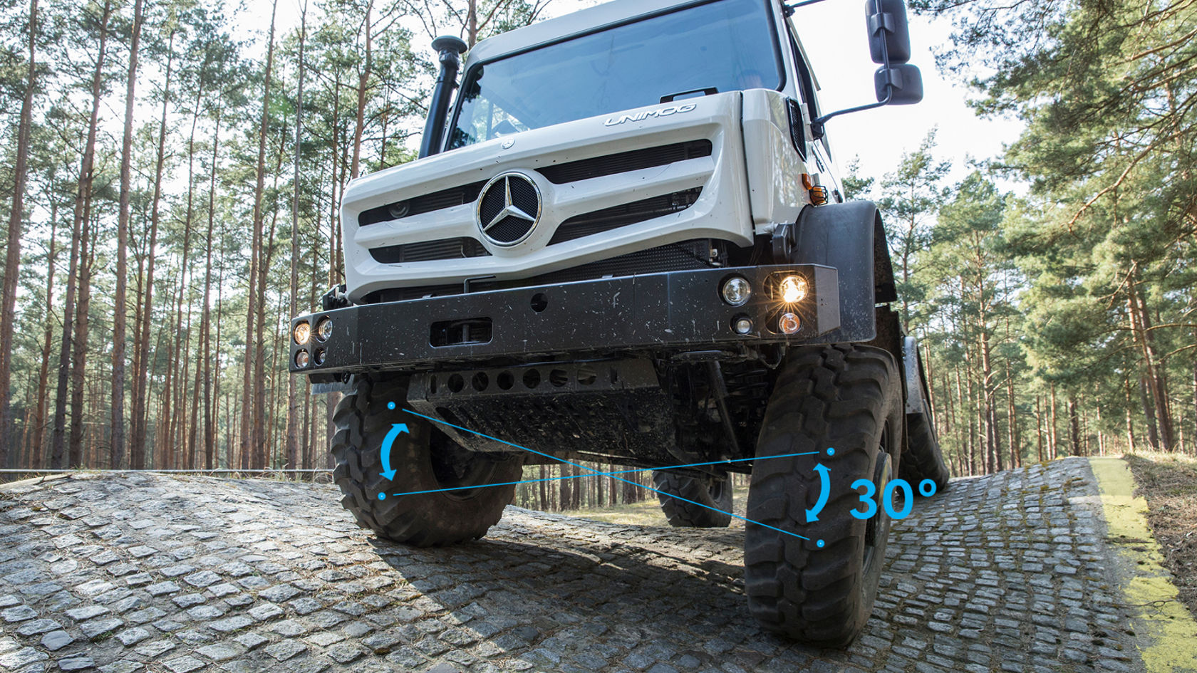 Un Unimog dimostra le sue capacità fuoristradistiche salendo su una ripida collina acciottolata in un’area boschiva.