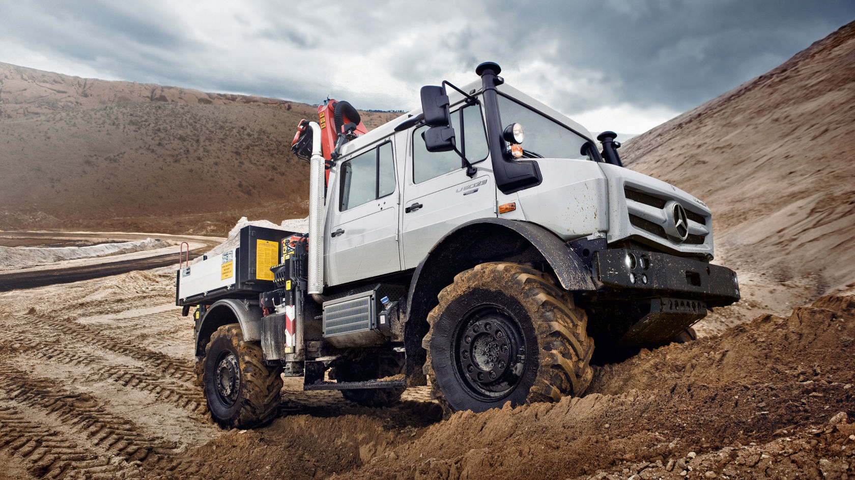 Ein weißer Unimog  fährt durch sandiges Gelände.