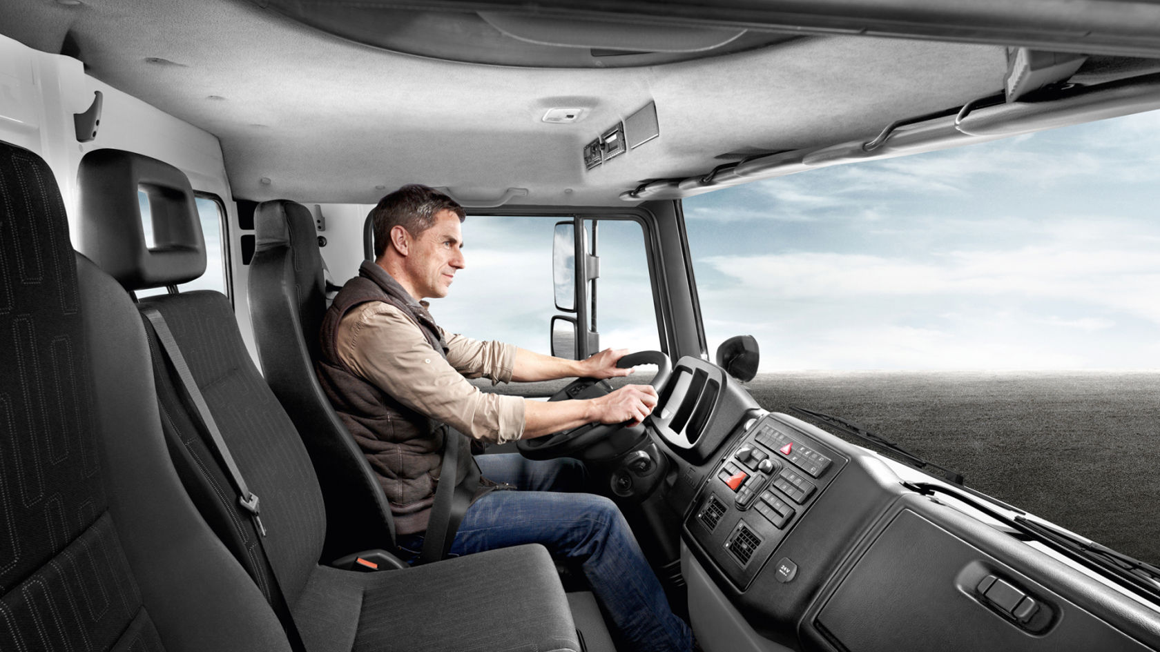 Coup d'œil dans la cabine d'un Unimog. Un homme est assis au volant et conduit le véhicule.