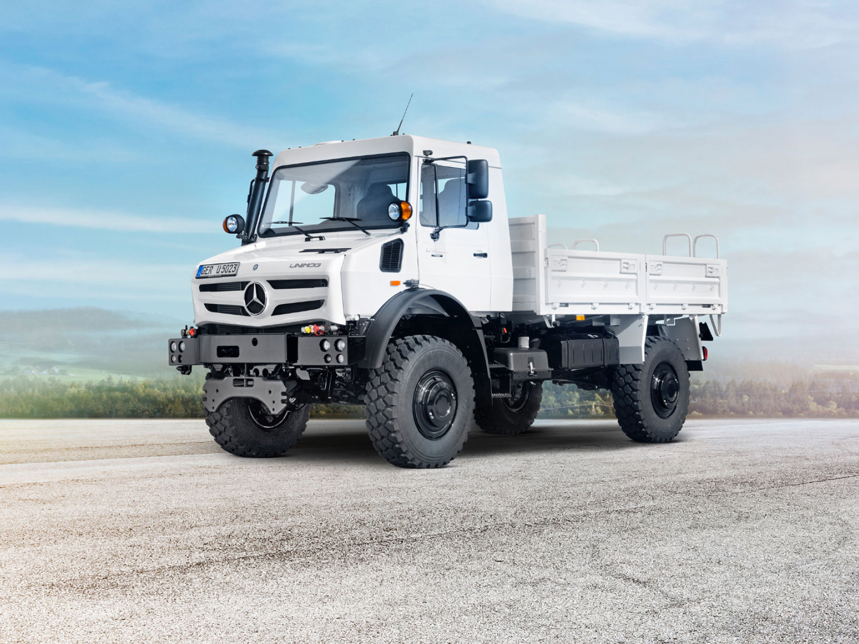 Ein weißer Unimog  steht auf einer Straße vor einem ländlichen Hintergrund.