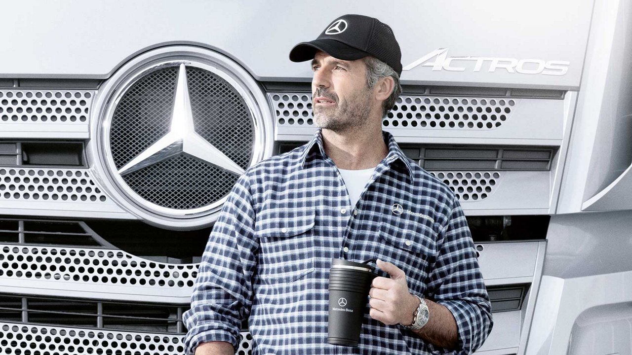 Een man voor zijn Mercedes-Benz Truck. Hij draagt een Mercedes-Benz pet en een Mercedes-Benz mok.