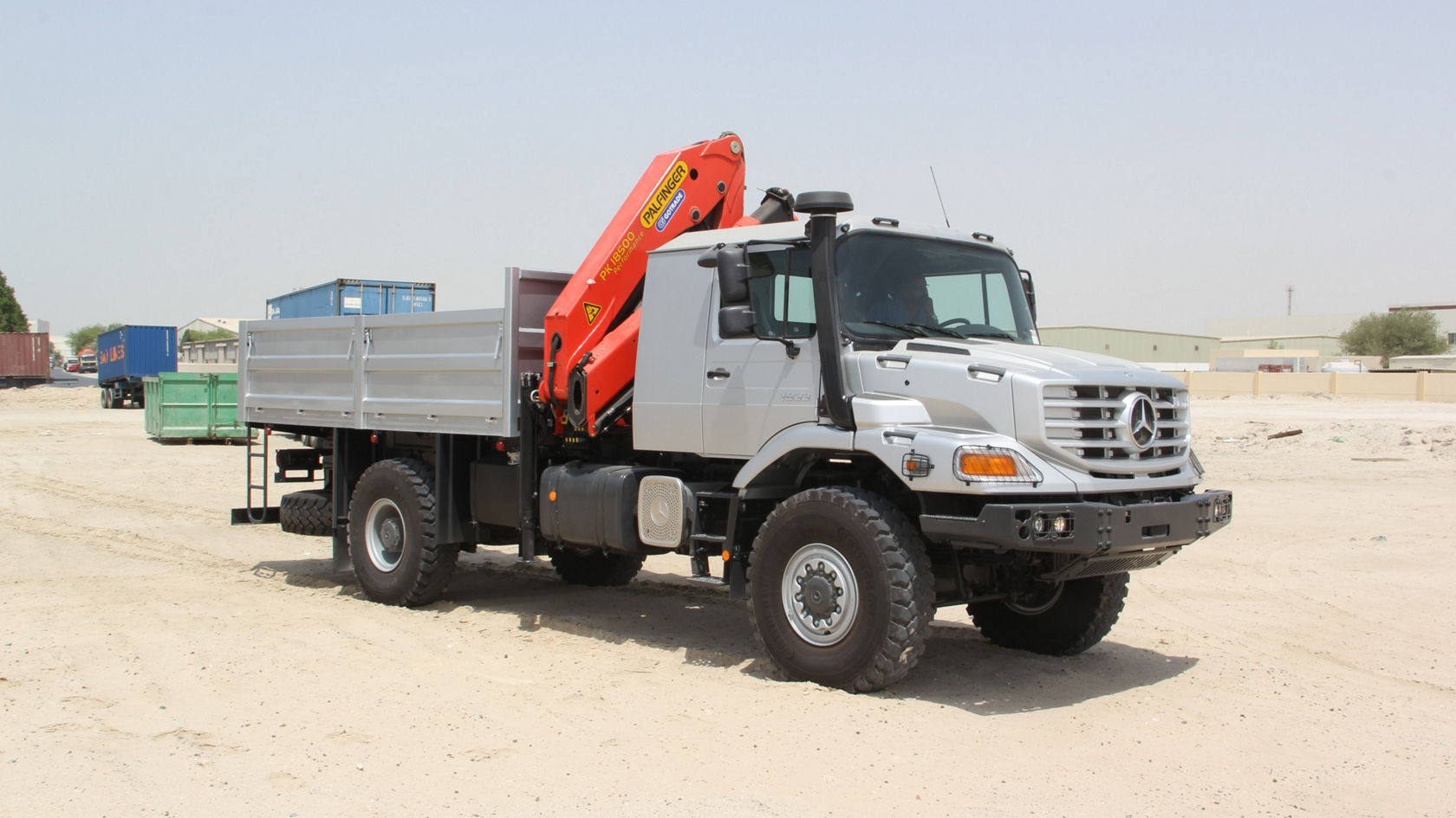 A Mercedes-Benz Zetros with a red crane body stands on sandy terrain. The truck has an open loading area and robust tyres, ideal for construction sites.