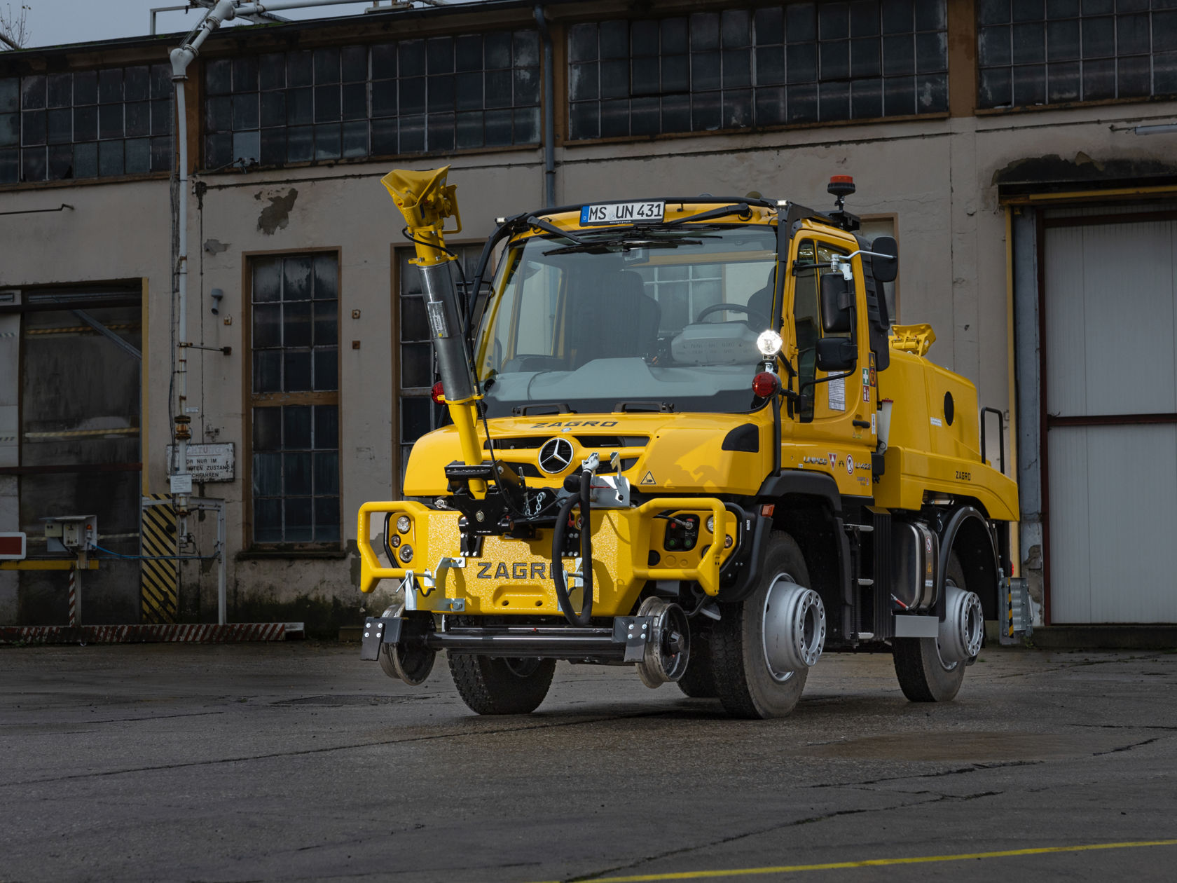 Kollane Unimog rööbastee varustusega, pargitud tööstushoone ette.