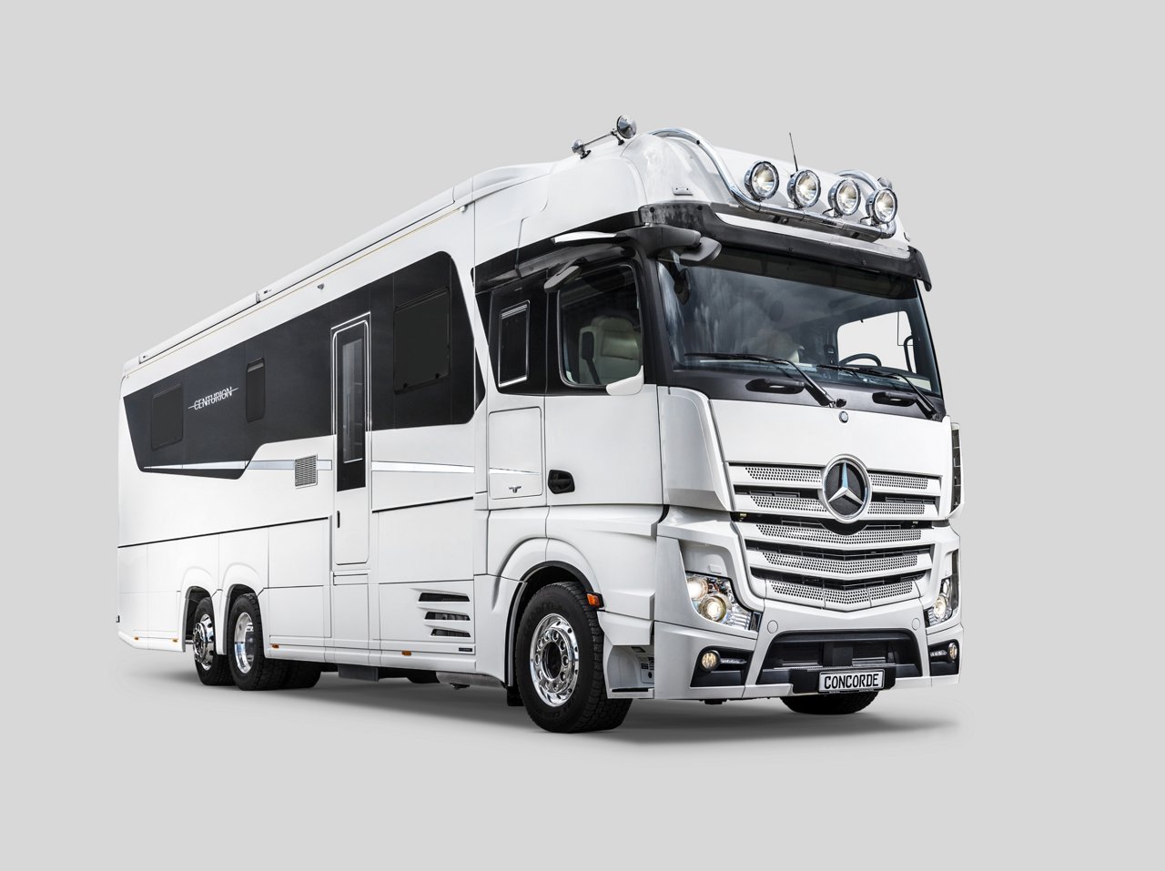 Das Bild zeigt einen weißen Actros als Concorde Centurion Reisemobil auf einem hellgrauen Hintergrund. Das Fahrzeug hat ein luxuriöses Design mit schwarzen Akzenten und Zusatzscheinwerfern auf dem Dach.