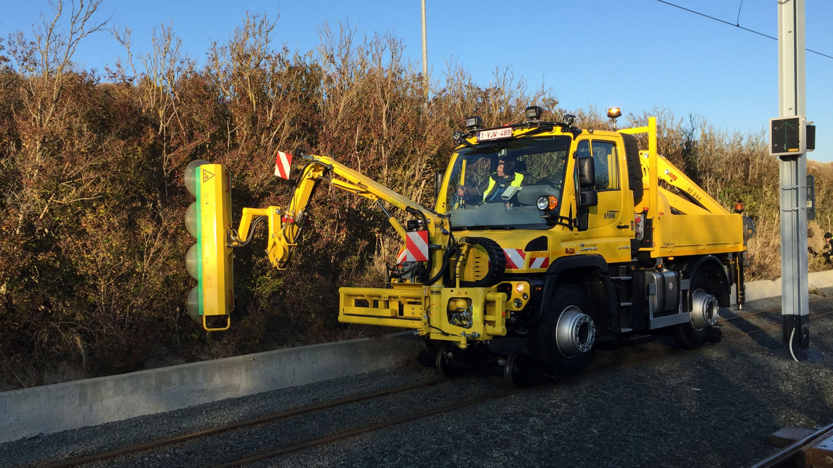 Rööbastee veermiku ja külgmise noolega kollane Unimog teeb hooldustöid piki raudteed asuval signaalseadmel.