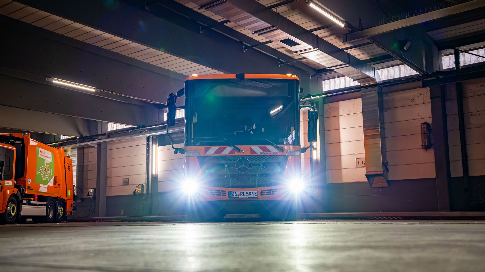 eEconic refuse collection vehicle with its headlamps on in the depot.