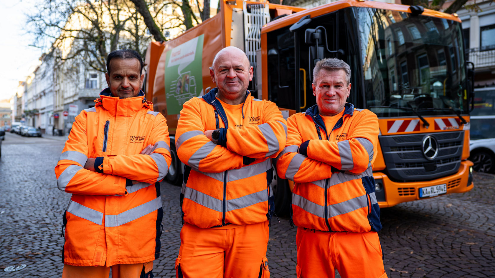 The waste collection team stands smiling with their arms folded in front of the eEconic.