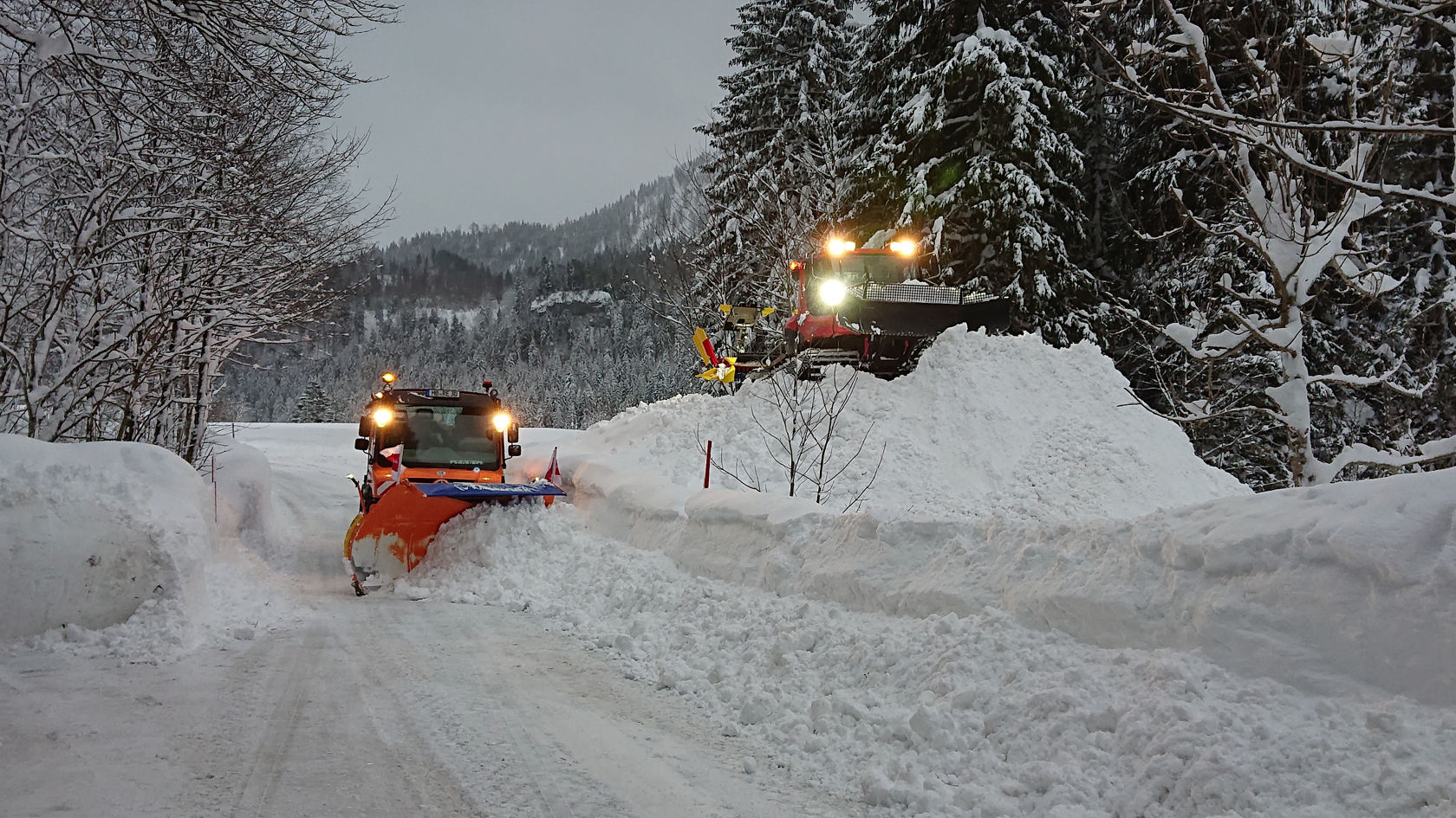 Unimog mit Schneepflug räumt tief verschneite Straße