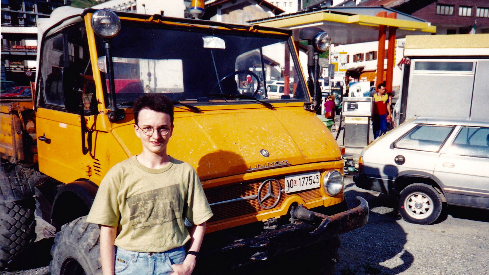 Ein Unimog von Mercedes-Benz in leuchtendem Gelb steht an einer Tankstelle, während eine Person daneben steht und in die Kamera schaut.