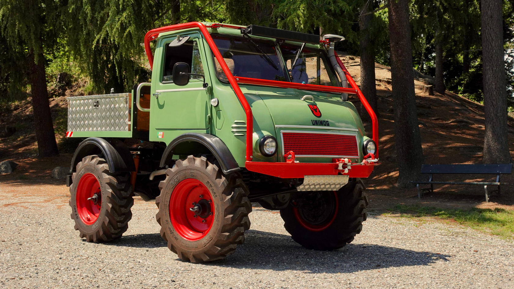 Robuster Mercedes-Benz Unimog im Freien, mit grüner Karosserie und rotem Rahmen, auf grobem Gelände mit großen Reifen, ideal für off-road Einsätze.