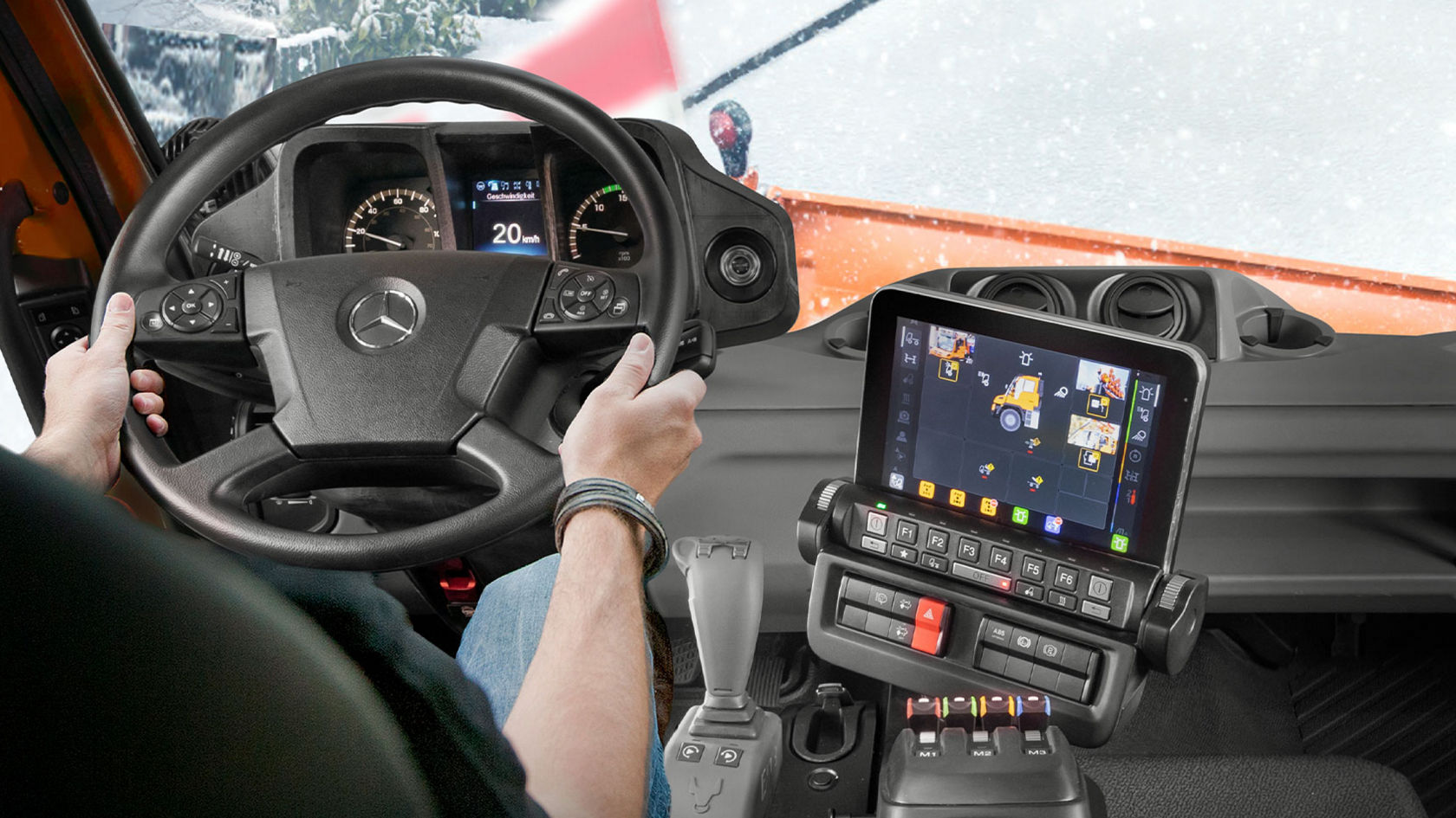 La vue du conducteur d'un porte-outils Unimog avec un écran affichant plusieurs perspectives de caméra. Le conducteur a les mains sur le volant et une route enneigée se trouve devant lui.