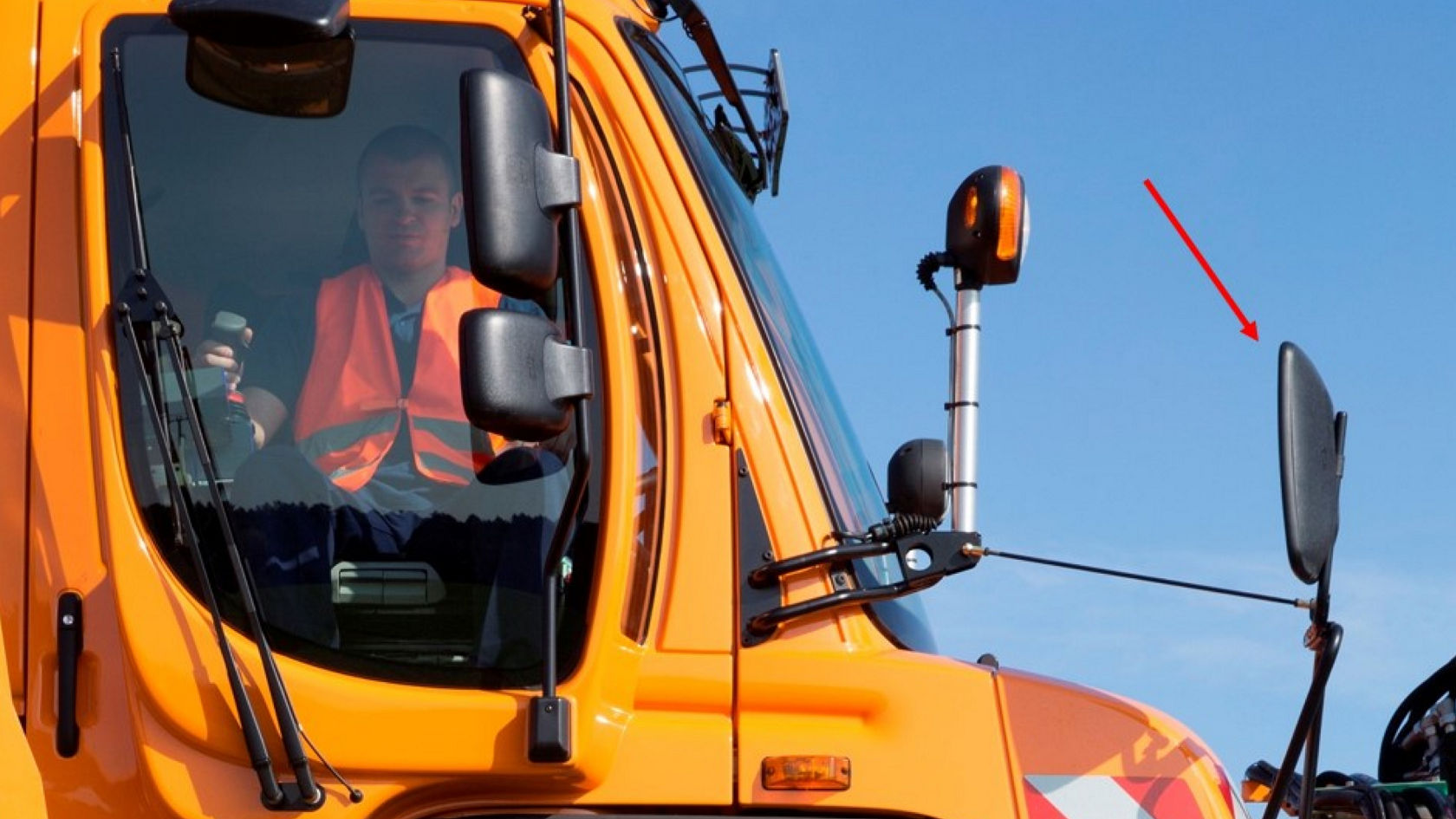 Le côté d'un porte-outils Unimog orange. Dans la cabine, on voit un conducteur portant un gilet de sécurité.