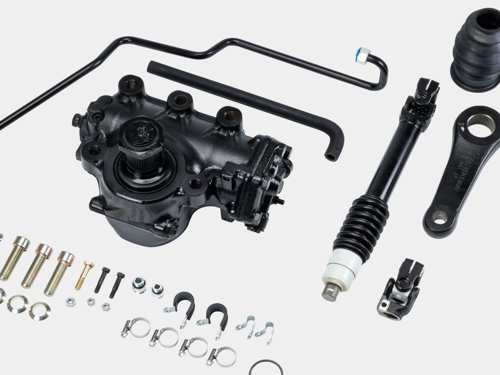 Various components of a steering system are spread out neatly on a white background. The parts are matt black and look brand new. Screws and nuts are next to them.