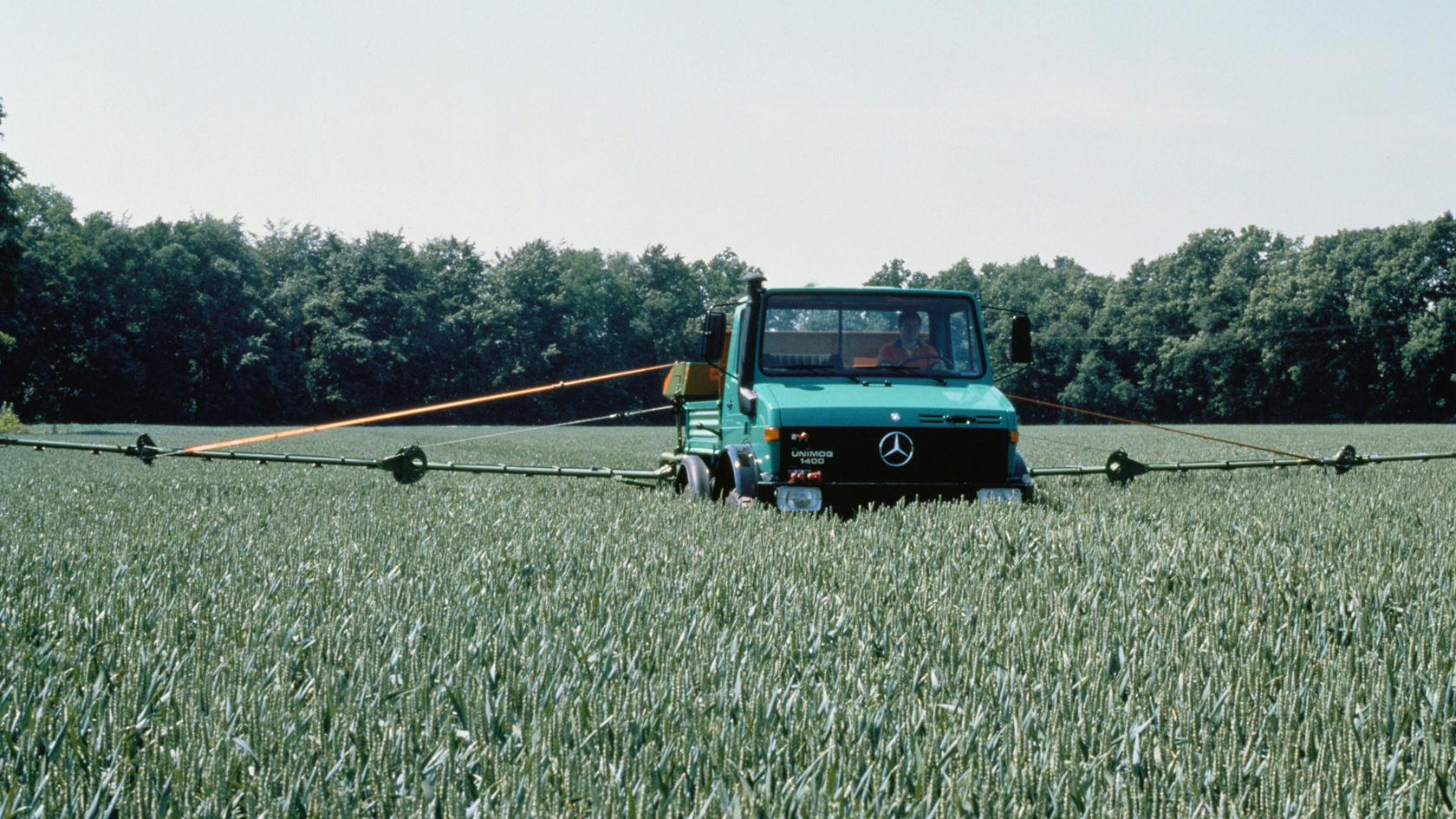 Een Unimog van Mercedes‑Benz staat in een veld, omringd door een grote spuitinstallatie die voor landbouwtoepassingen wordt gebruikt.