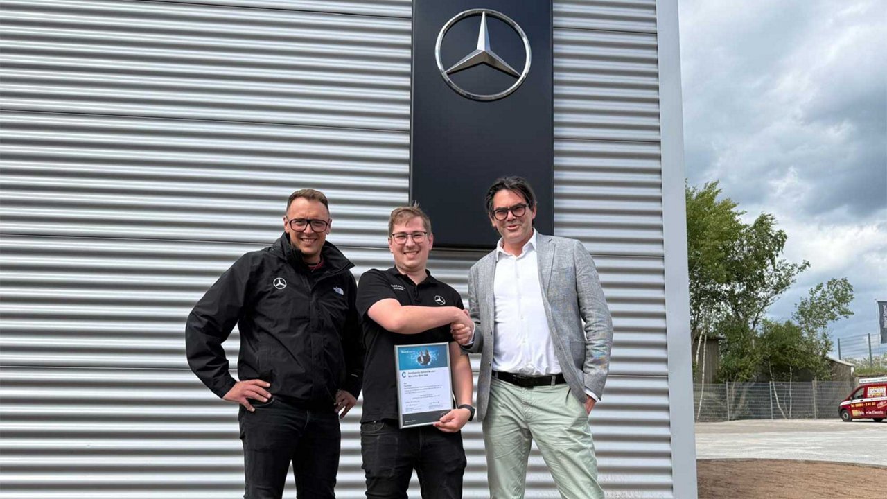 Der Mitarbeiter Paul Burger hält eine Urkunde in Händen. Rechts daneben steht der Geschäftsführer Herr Lukas Haag, links daneben Herr Sven Perius.