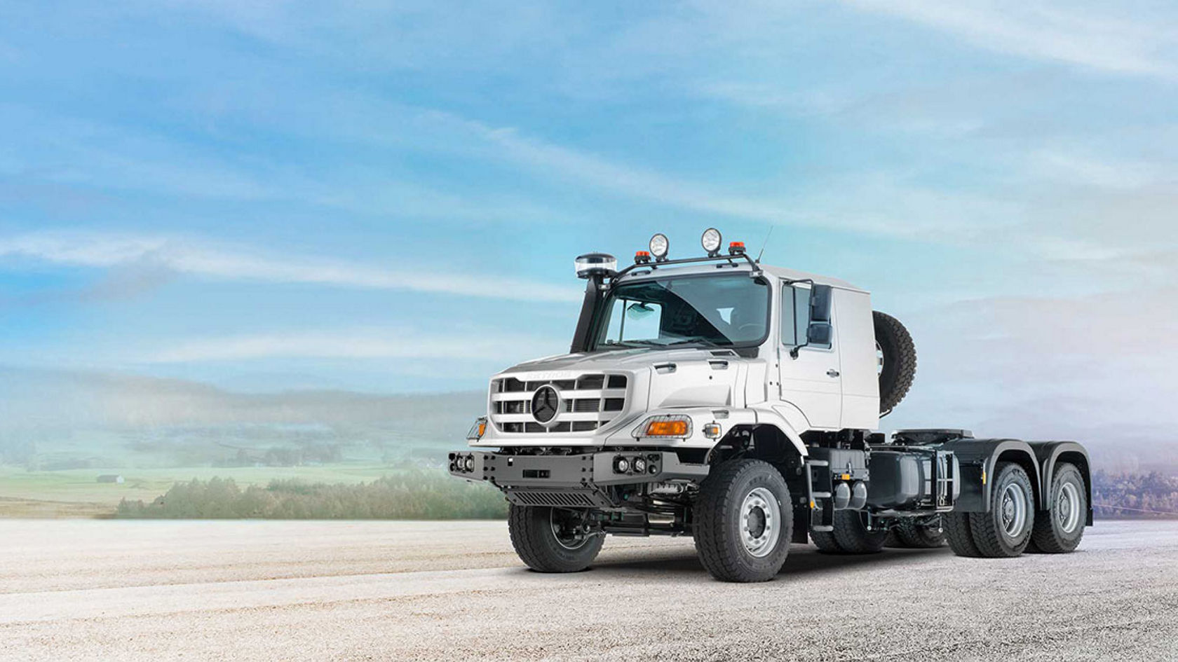 A silver Zetros stands on a wide, flat surface against a background of blue sky and distant mountains.